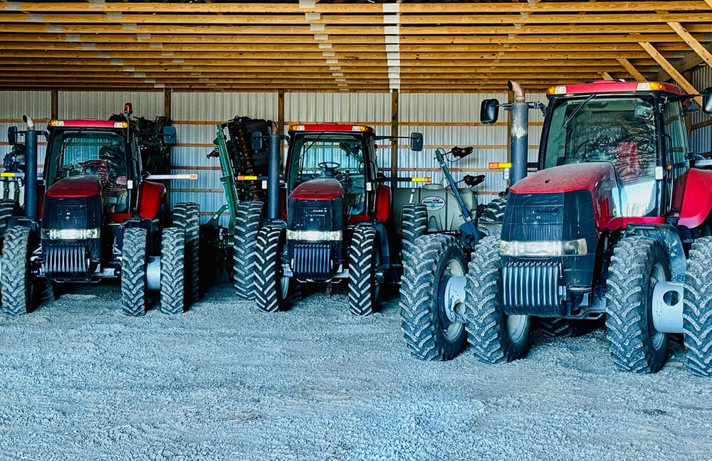 A barn that has three Case IH tractor inside with tillage and spraying equipment